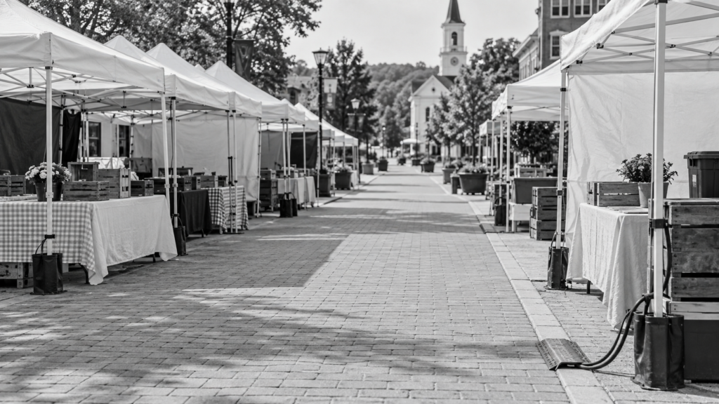 Black-and-white empty outdoor fair with vendor tents beside a pedestrian walkway
