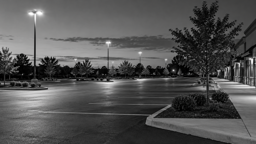 Parking-lot lighting illuminating an empty shopping-center lot and pedestrian curb