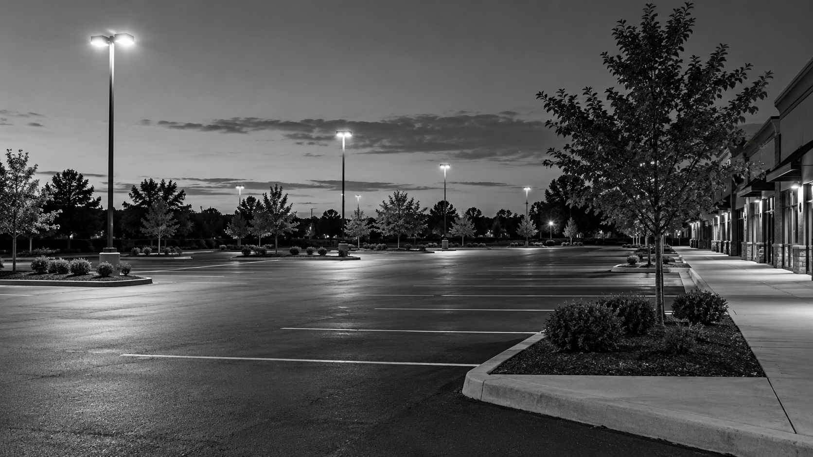 Parking-lot lighting illuminating an empty shopping-center lot and pedestrian curb