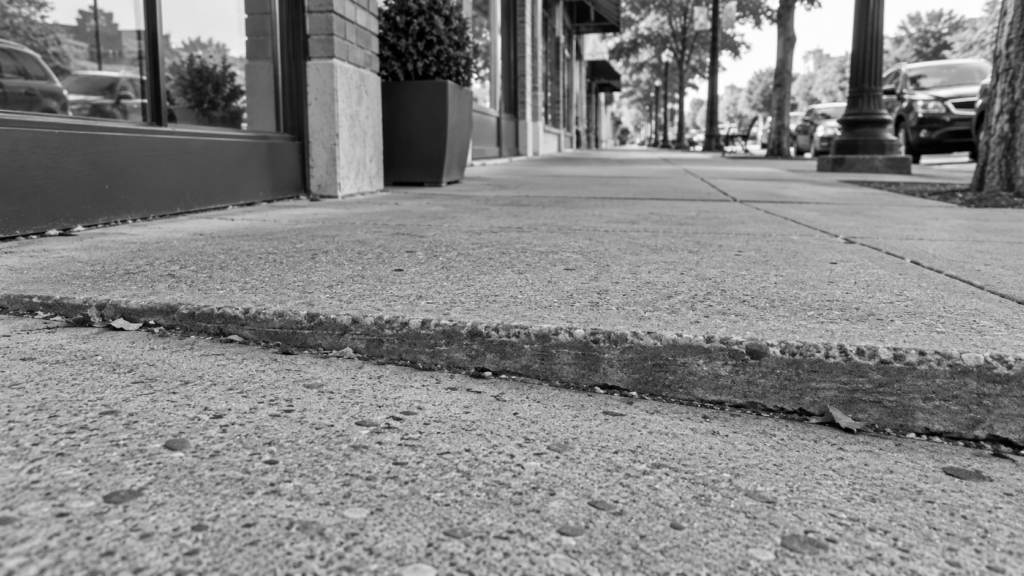 Public sidewalk with a raised concrete joint beside commercial storefronts