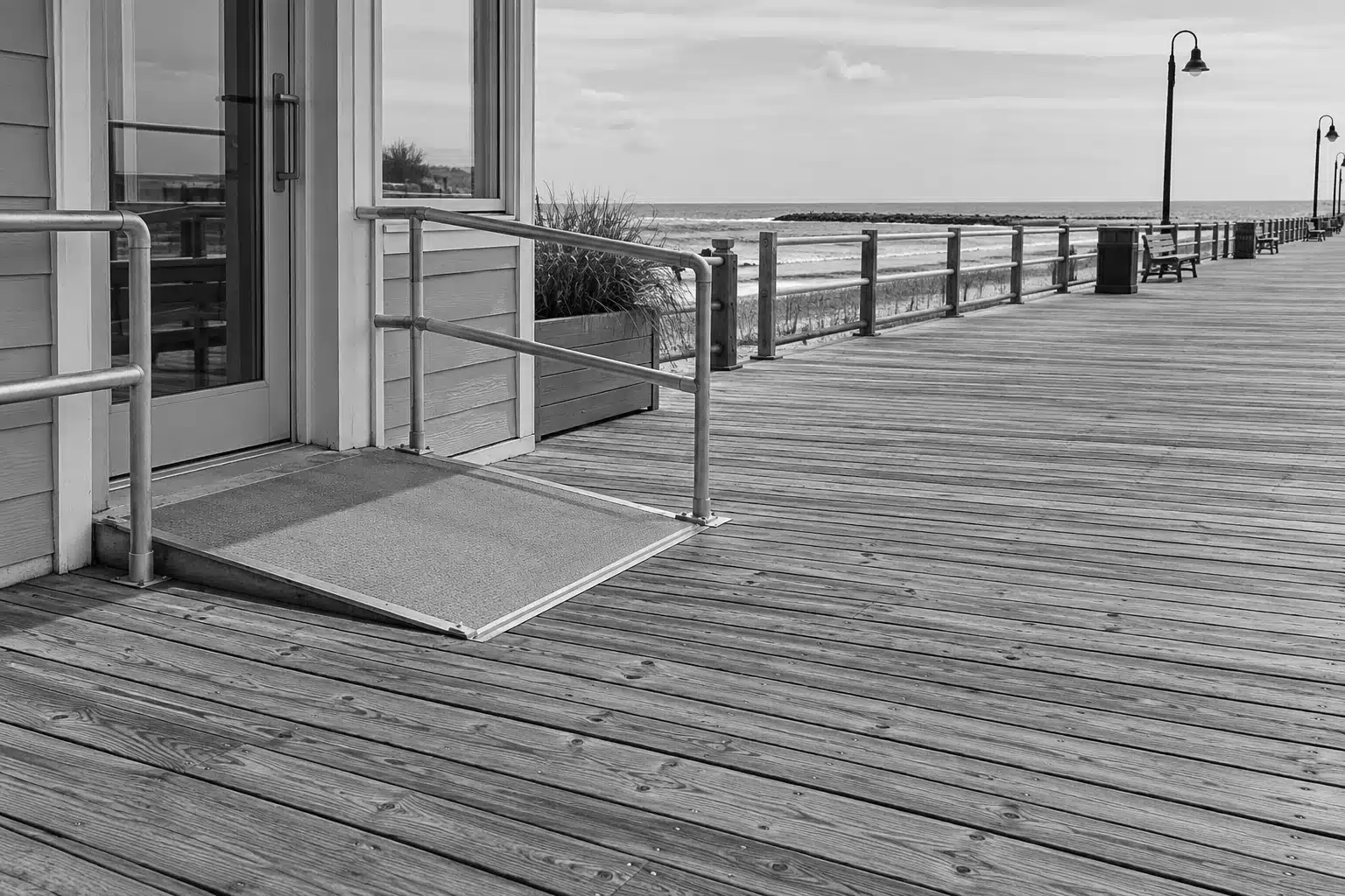 Empty seaside boardwalk with a ramp and railings near storefronts